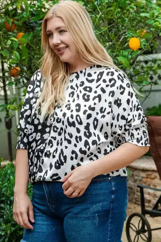Smiling model wearing black and white leopard print plus size blouse with smocked sleeves, perfect for summer outings.