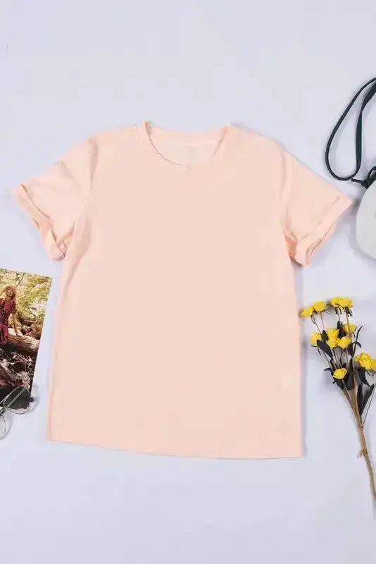 Flat lay of light pink plus size T-shirt with rolled sleeves, styled with floral accessories and sunglasses for a soft casual vibe.