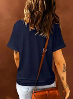 Back view of navy blue plus size T-shirt with rolled sleeves, paired with light denim jeans and a brown crossbody bag.