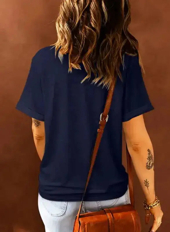 Back view of navy blue plus size T-shirt with rolled sleeves, paired with light denim jeans and a brown crossbody bag.