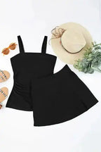 Flat lay of black square neck tankini swimsuit set with top and skirt, styled with summer accessories for vacation wear.