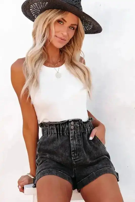 Model wearing black vintage washed denim shorts with high waist frilled hem, paired with a white tank top for a chic summer look.