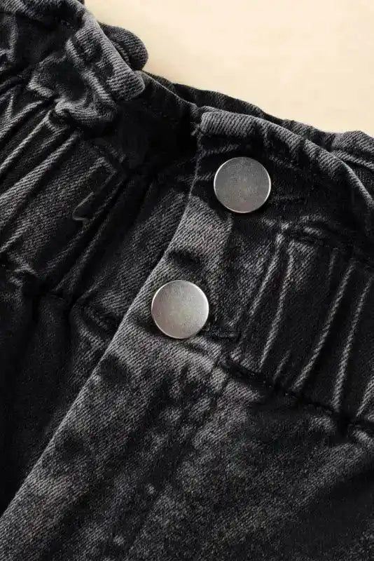 Detail of high waist frilled hem and double button closure on black vintage washed denim shorts, highlighting the waistband design.