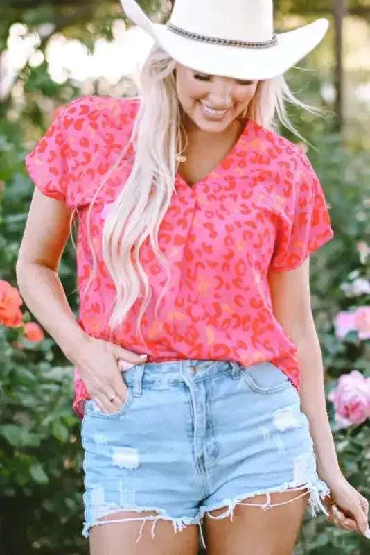 Wild in Pink Leopard Blouse with short sleeves and V-neck worn outdoors with distressed shorts. Vibrant pink top ideal for summer western style.