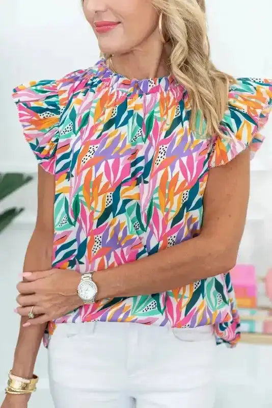 Pink Floral Flutter Sleeve Blouse with vibrant multicolor print and ruffle neckline, styled for summer wear with white pants.