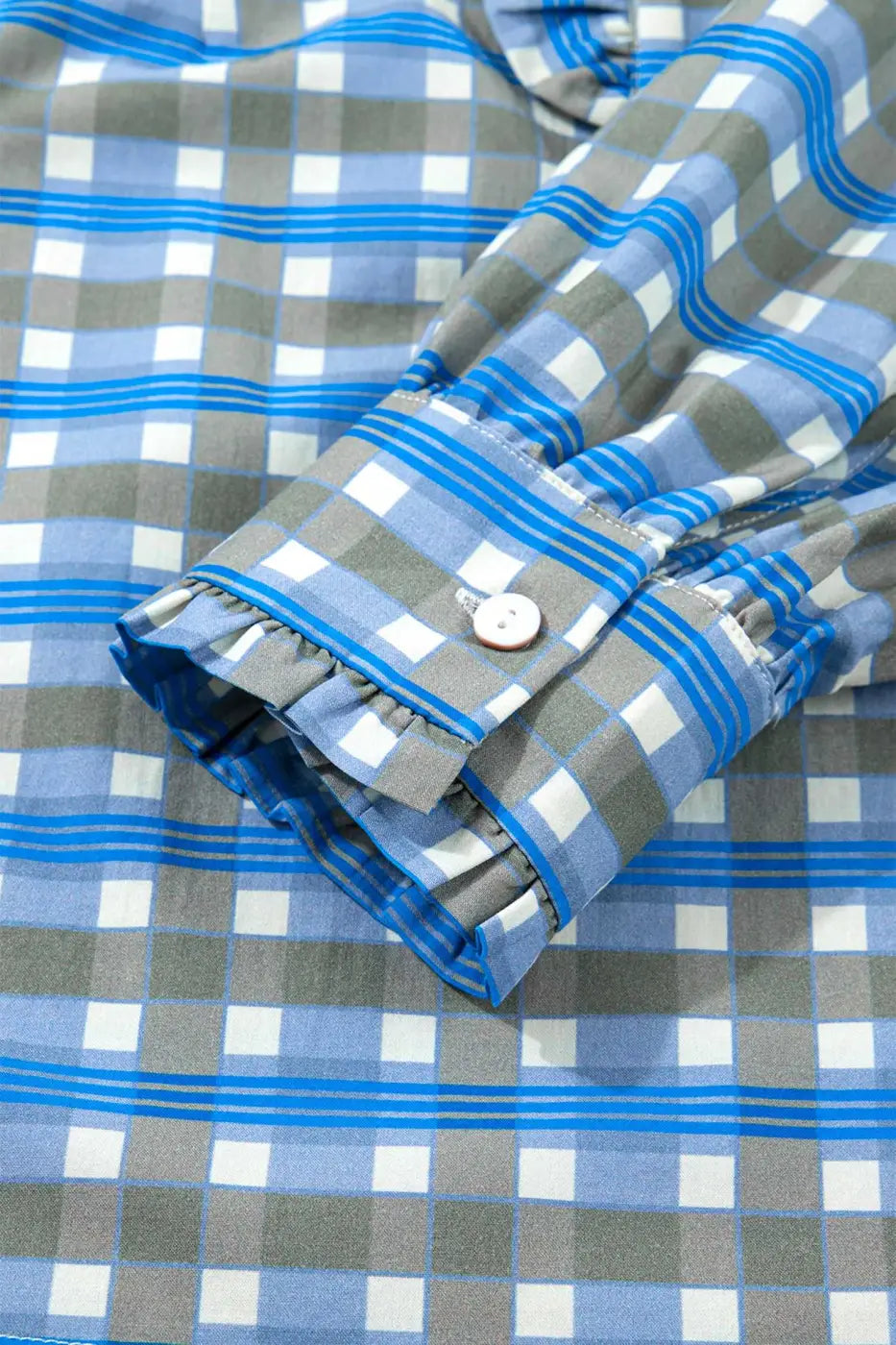 Detail of cuff on blue plaid long sleeve frilled blouse with button closure and subtle ruffle trim in soft cotton fabric.