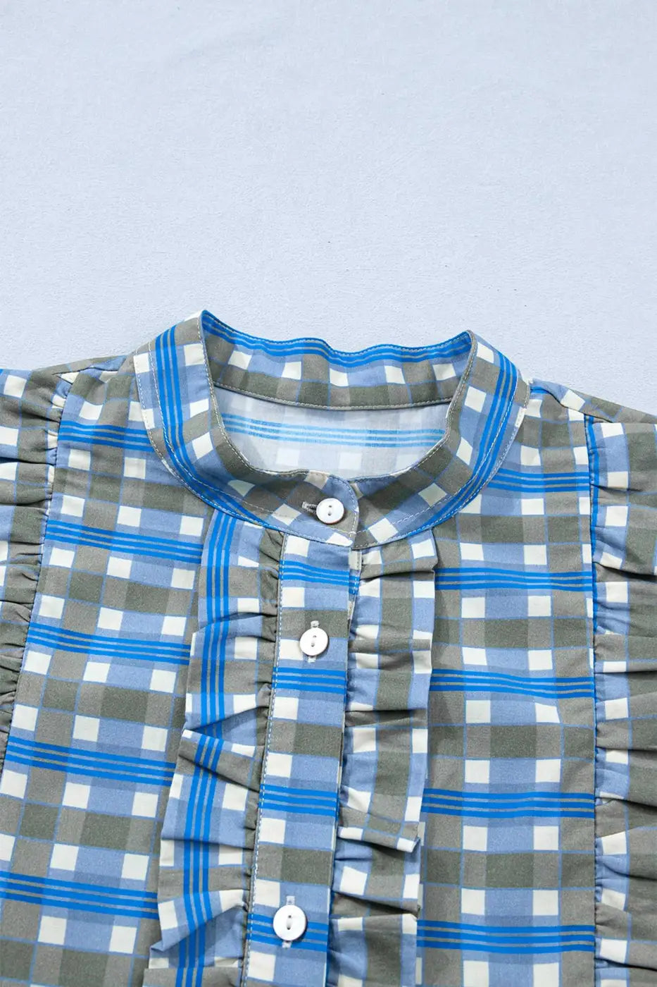 Close-up of blue plaid long sleeve frilled blouse showing front button placket and ruffled detailing on soft cotton fabric.