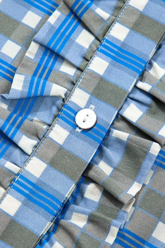 Close-up of frilled front and white button on blue plaid cotton blouse, showcasing half-button design and soft fabric texture.
