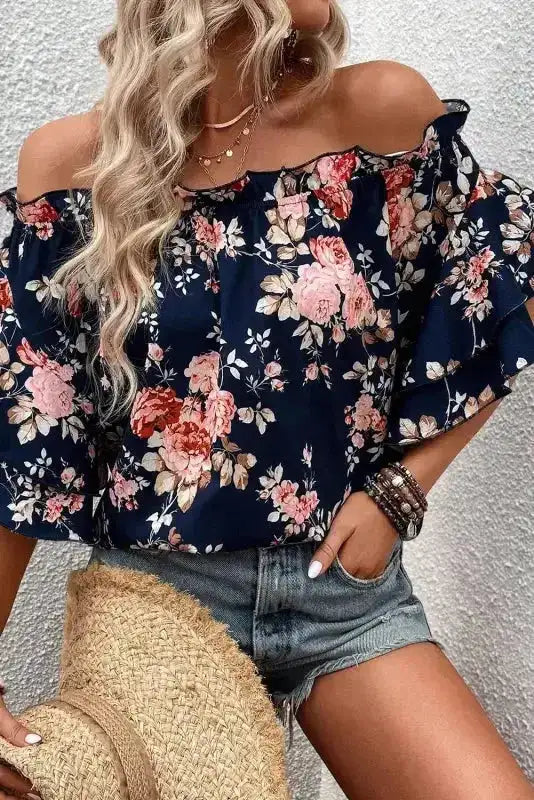 Blue floral off‑shoulder blouse with flounce sleeves, paired with denim shorts and straw hat, ideal for warm-weather casual style.