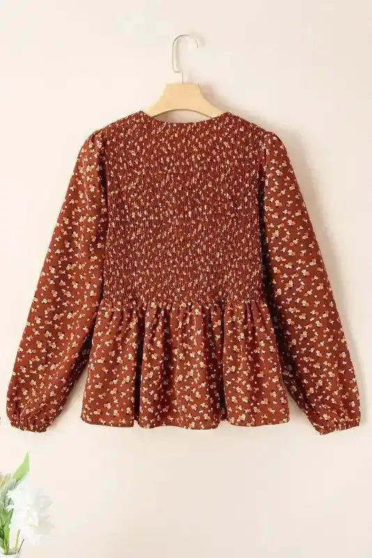 Back view of Boho Floral Peplum Blouse on hanger, featuring smocked detail and long sleeves in floral fabric.