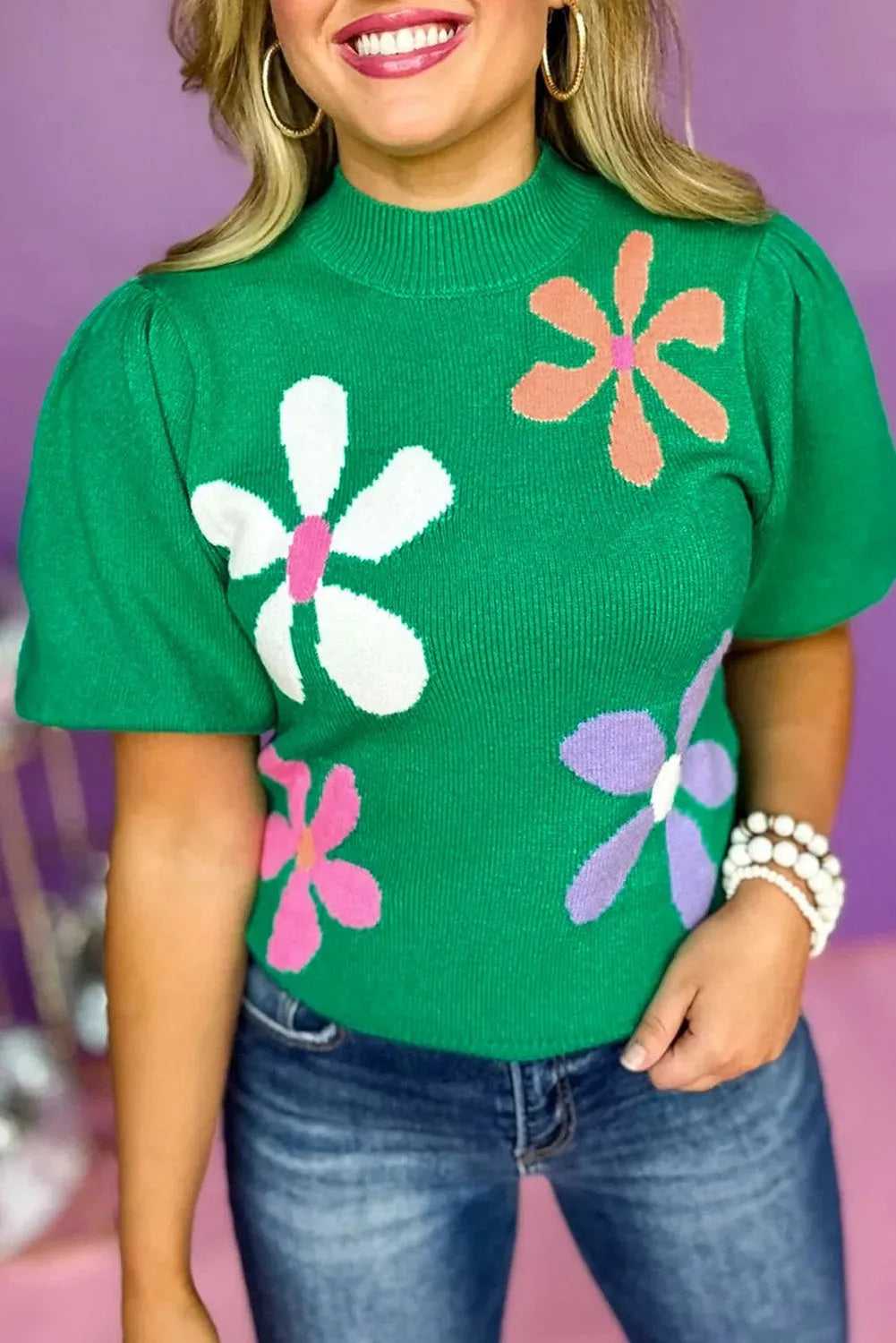 Ladies bright green floral sweater with bubble short sleeves, featuring large colorful flower prints, styled with denim jeans.