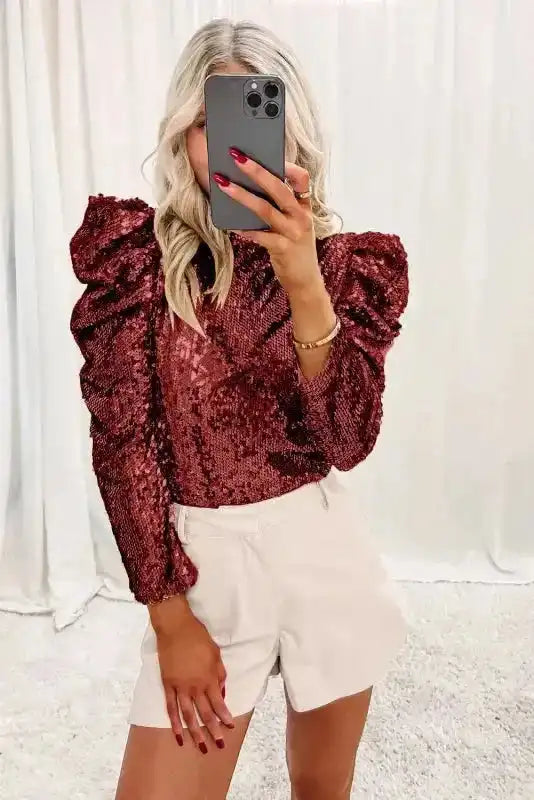 Fashion-forward Burgundy Sequin Mock Neck Top with dramatic bubble sleeves, styled with neutral shorts for a chic holiday look.