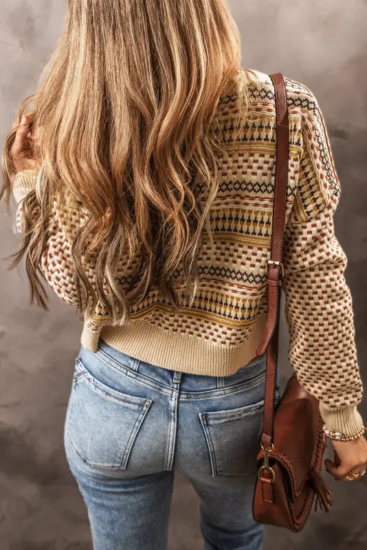 Patterned beige sweater worn with blue jeans, brown leather bag, buttoned cropped cardigan