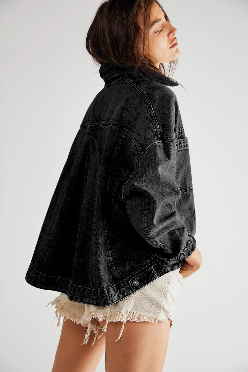 Person wearing a black denim jacket and white shorts on a plain background