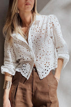 Woman wearing a white lace blouse with brown pants against a neutral background