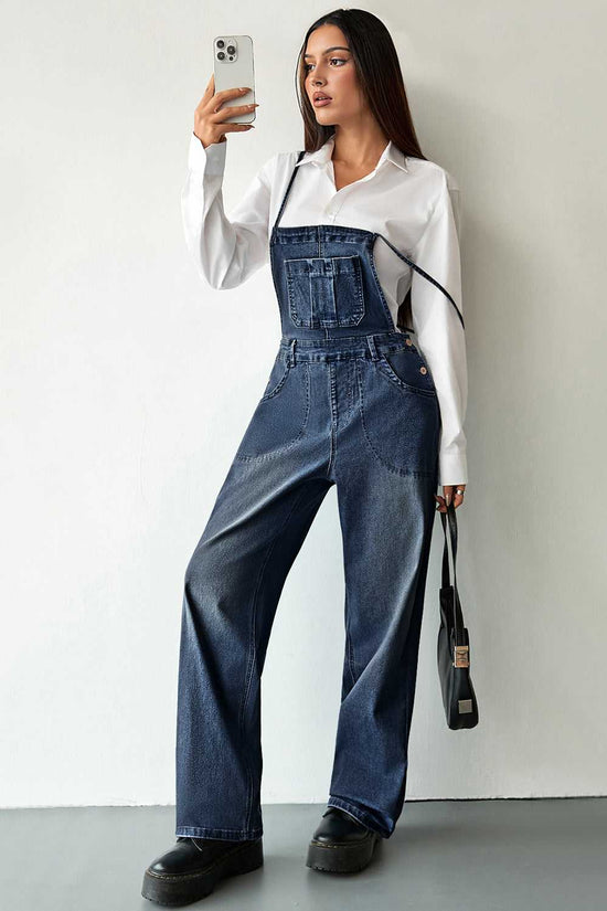 Dark blue baggy denim overalls for women styled with a white shirt and black boots. Relaxed fit with front pocket and adjustable straps.
