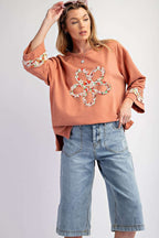 Model wearing Flower Patch Graphic Top with floral applique and wide sleeves, paired with denim bermuda shorts for a Southern Belle style.