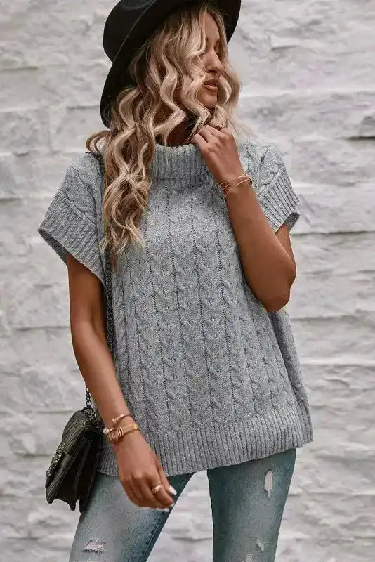 Model wearing grey cable knit turtleneck short sleeve jumper with hat and jeans. A modern casual knitwear piece for women.