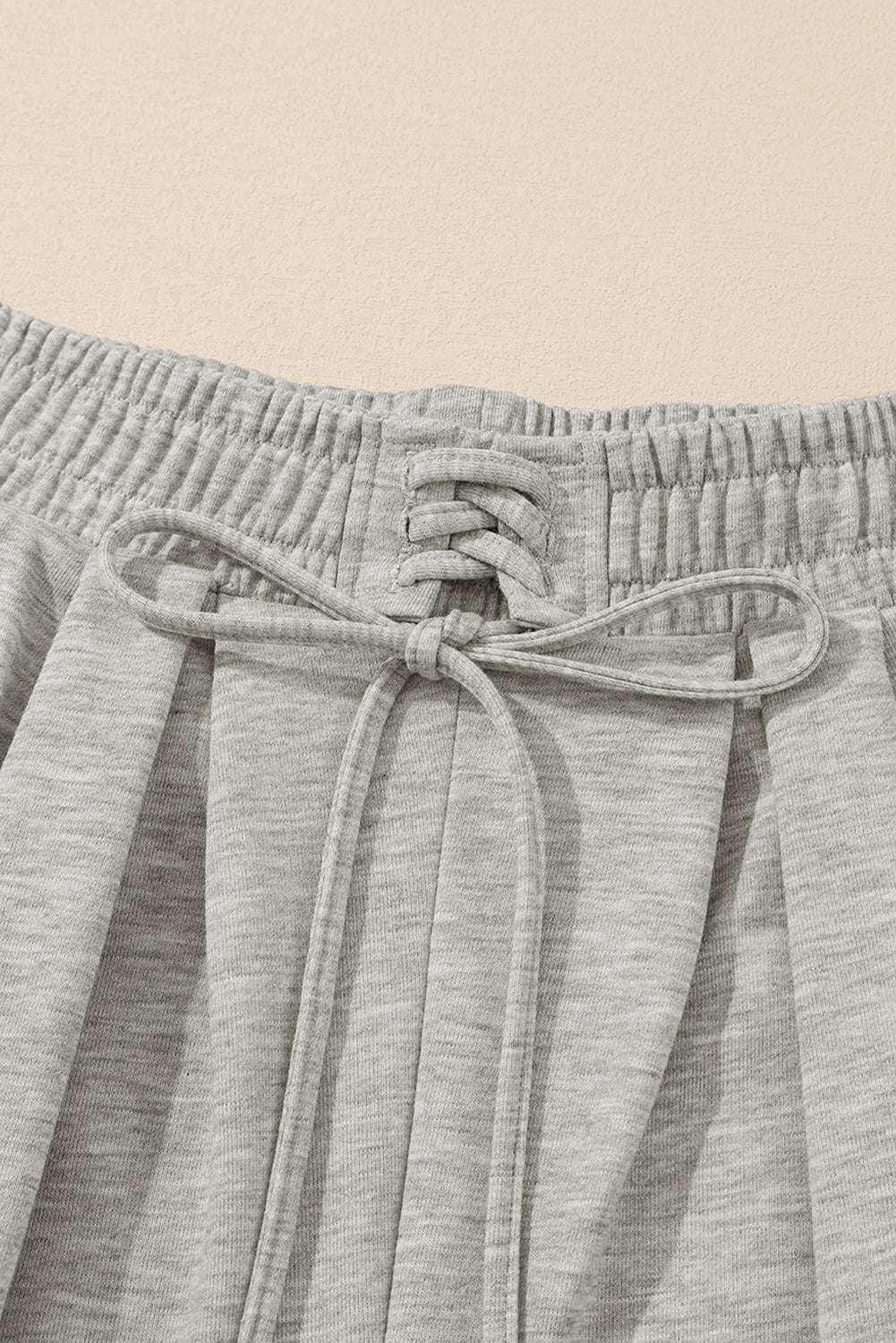 Close-up of gray pleated sweatpants waistband with drawstring and pleat detailing, highlighting comfort and design.