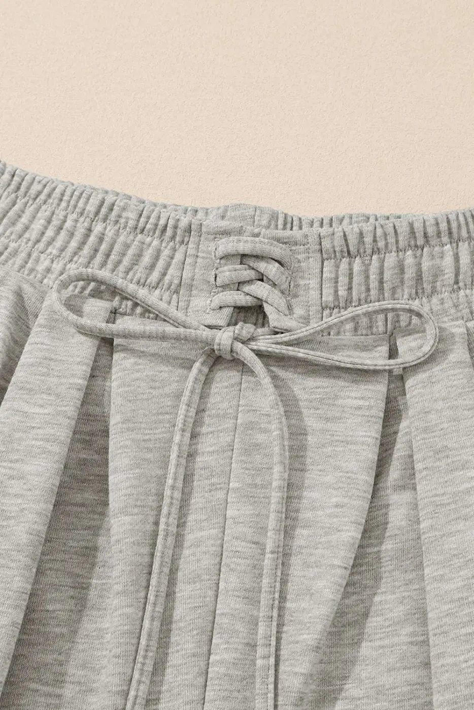 Close-up of gray pleated sweatpants waistband with drawstring and pleat detailing, highlighting comfort and design.