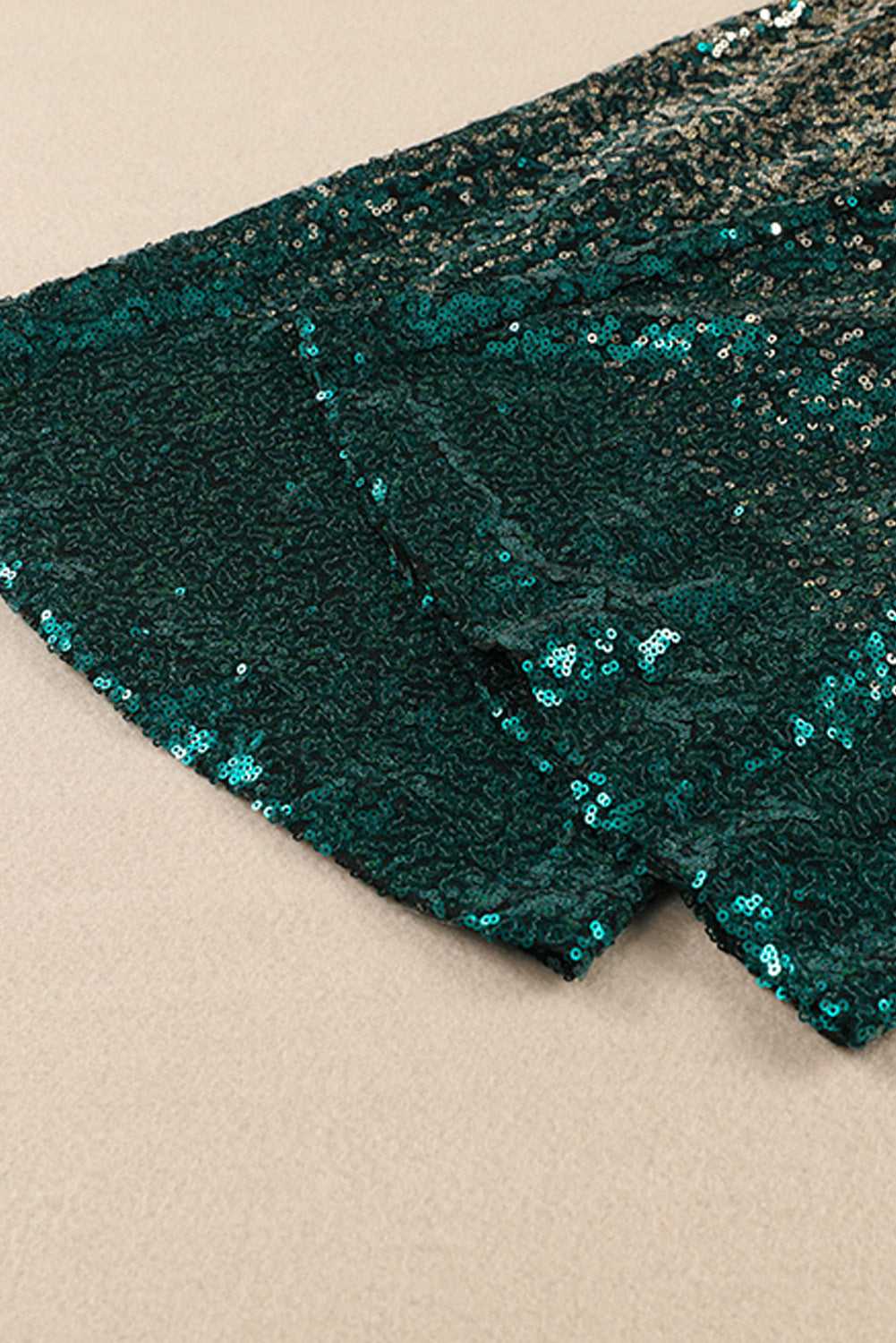 Close-up of flared hem on green and gold sequin trousers. Detailed view of shimmering sequin texture and elegant flare.