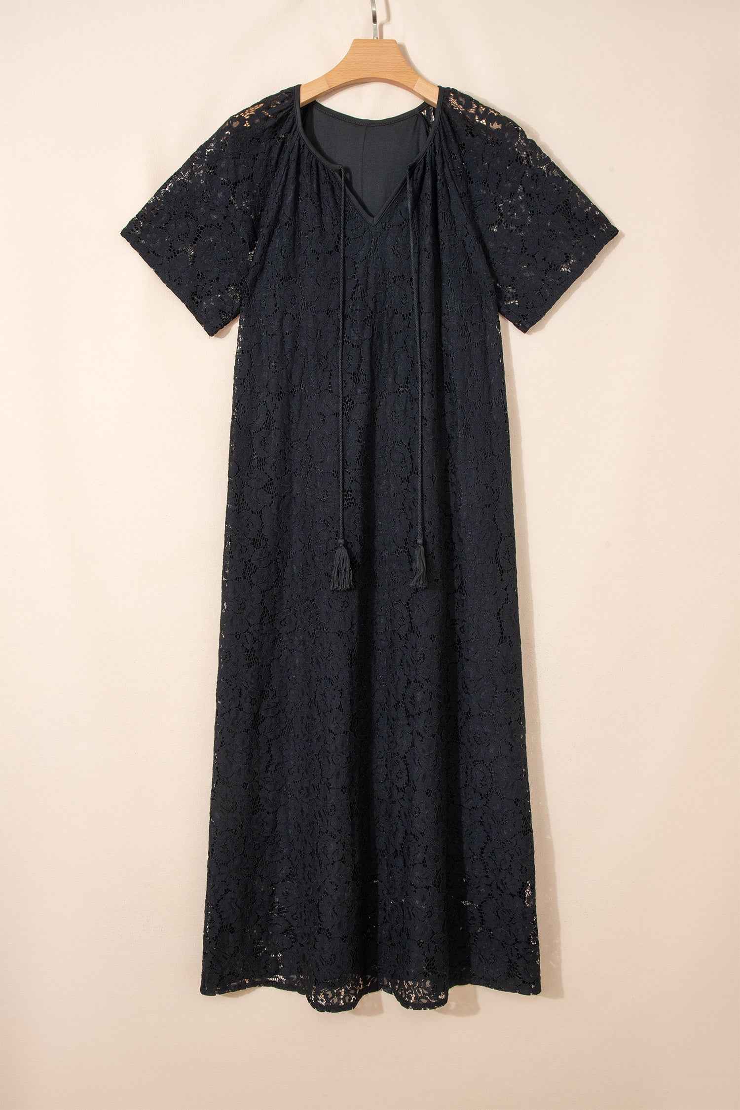 Black Lace Overlay Maxi Sundress displayed on hanger, featuring short sleeves, tassel tie neckline, and elegant floral lace fabric.