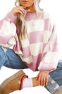 Person wearing a pink and white checkered sweater and blue jeans, sitting on a white surface.