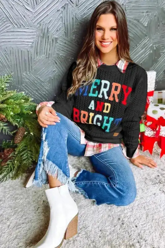 Holiday-themed black sweatshirt with 'MERRY AND BRIGHT' chenille embroidery, styled with denim and boots for seasonal fashion.