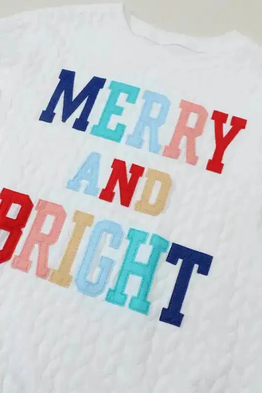 Detail view of 'MERRY AND BRIGHT' chenille embroidery on white sweatshirt, highlighting vibrant holiday-themed lettering.