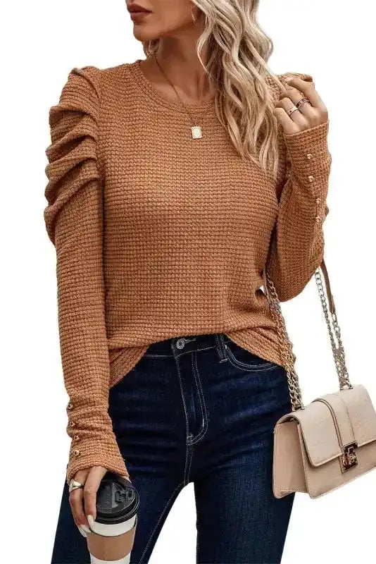 Studio view of FashionFitz Chestnut Textured Top with gigot sleeves and gold button details, paired with dark jeans and a beige chain purse.
