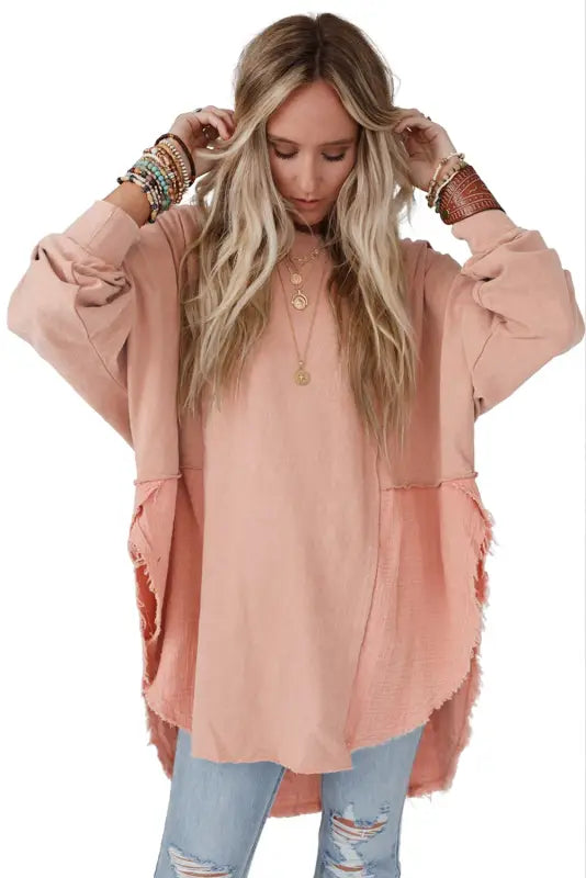 Chic high-low hem oversized blouse with frayed edges and exposed seam, worn over distressed jeans