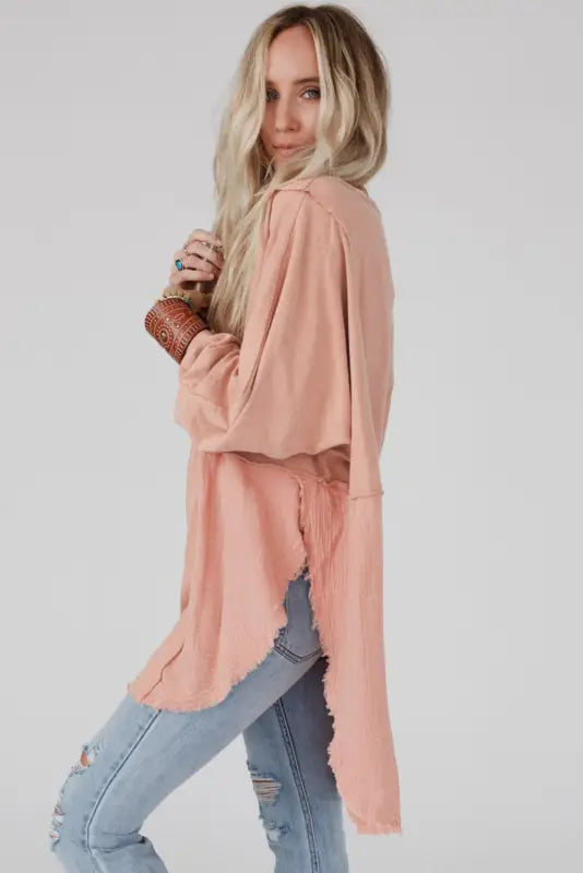 Woman with long blonde hair in peach oversized sweater, ripped jeans with exposed seam design