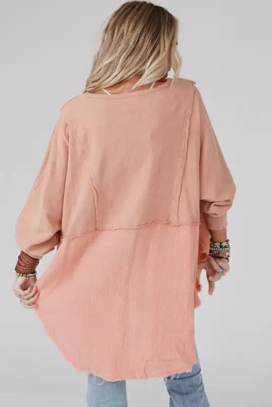 Blonde wearing chic high-low hem oversized blouse in pink with exposed seam design, rear view