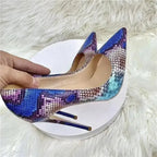 Hand holding Cobalt Viper Snake Heels with sharp pointed toe and high stiletto heel, emphasizing the bold snake print design.