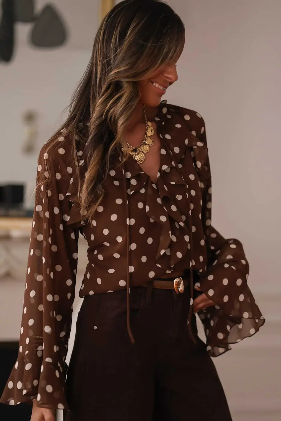 Coffee polka dot bell sleeve blouse for women with tie neck and ruffled details, styled with high-waisted trousers for an elegant office look.