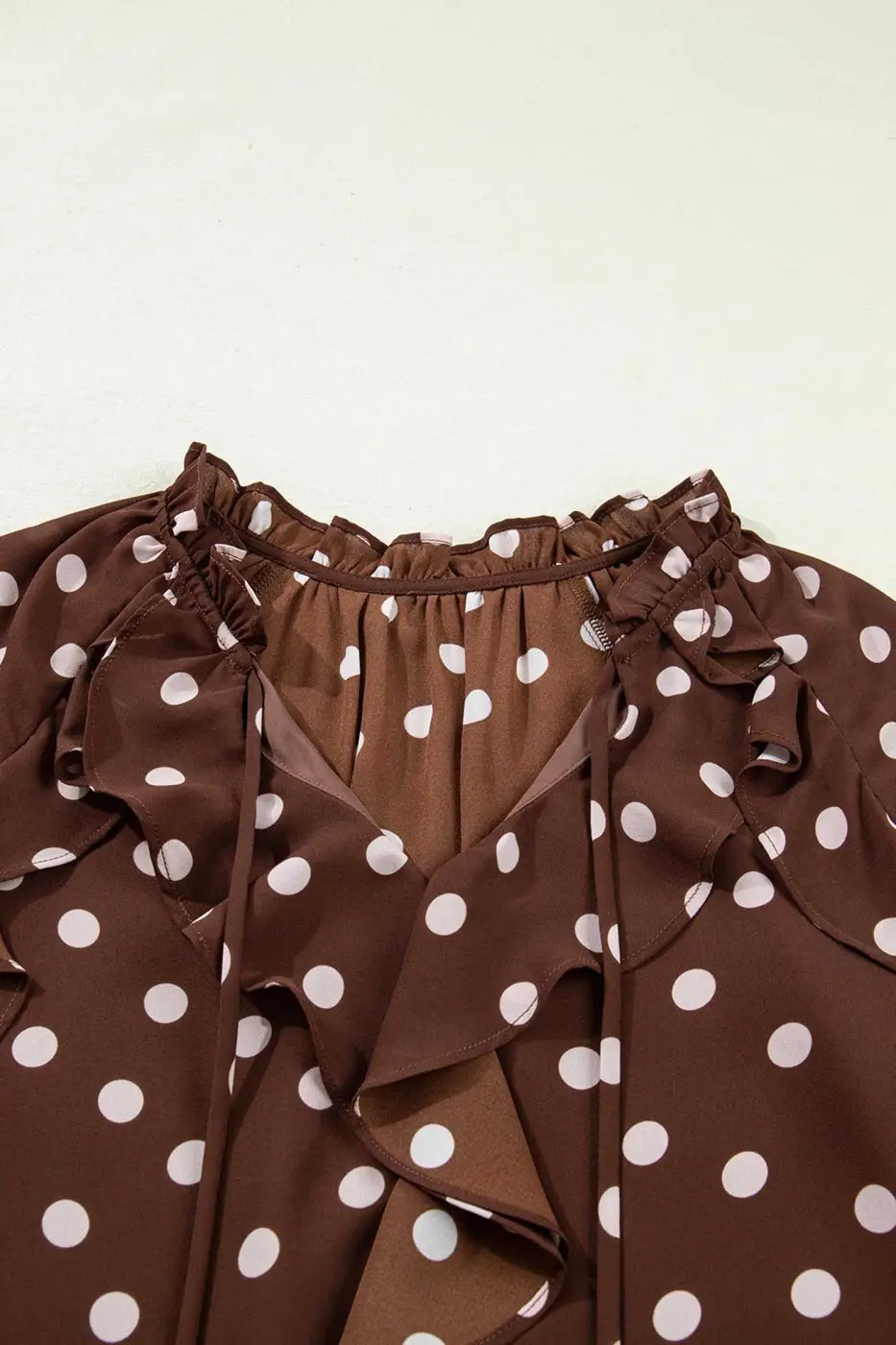 Close-up of the neckline on the coffee polka dot bell sleeve blouse, featuring a chiffon tie neck and soft ruffle trim for a feminine touch.