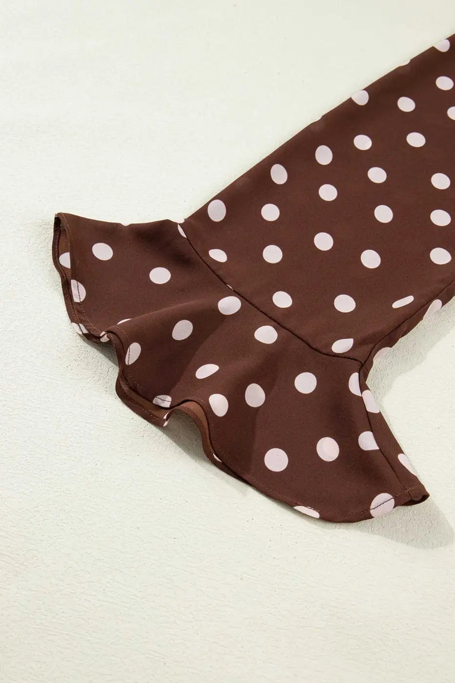 Detail of the bell sleeve on the coffee polka dot blouse, showcasing the flared ruffle cuff in lightweight chiffon fabric.