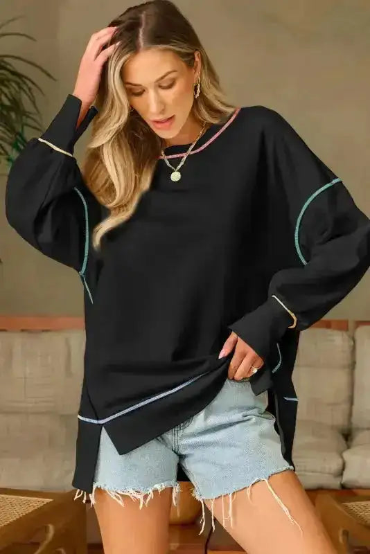 Black oversized sweatshirt with colorful contrast seams and split hem, styled with denim shorts for a casual chic look.