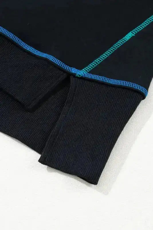 Close-up of black sweatshirt's ribbed cuff and colorful seam detailing, highlighting quality craftsmanship and split hem design.