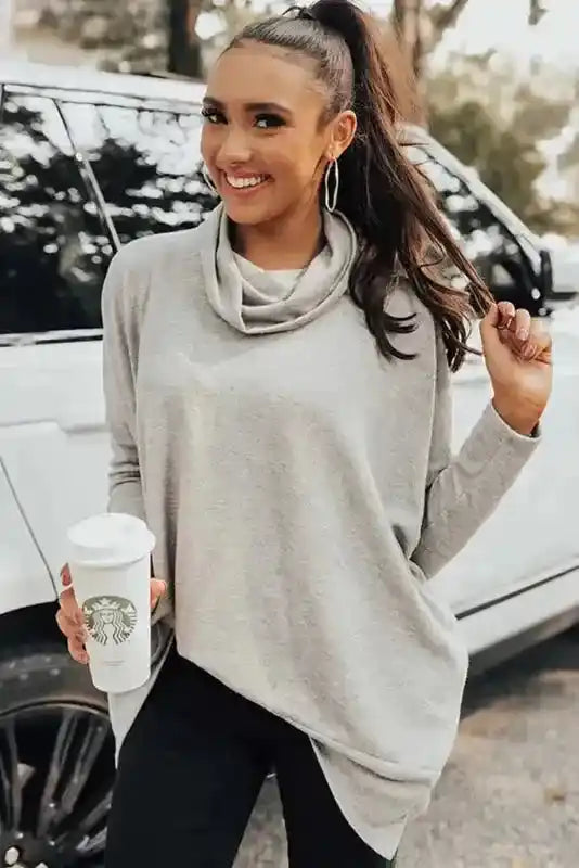 Smiling model in gray Cowl Neck Shift Tunic Top holding a coffee cup, styled for a relaxed and fashionable winter look.