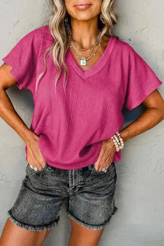 Crinkled V-Neck T-Shirt in vibrant pink with wide sleeves, styled casually with denim shorts for summer wear.