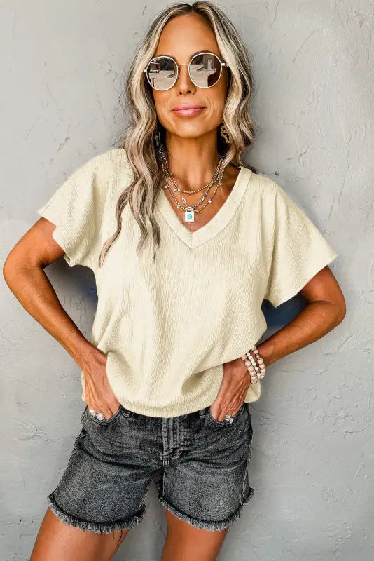 Woman relaxing in crinkled v-neck t-shirt, sunglasses, denim shorts, and layered accessories