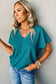 Woman with blonde hair in teal top, layered jewelry, modeling crinkled v neck t-shirt