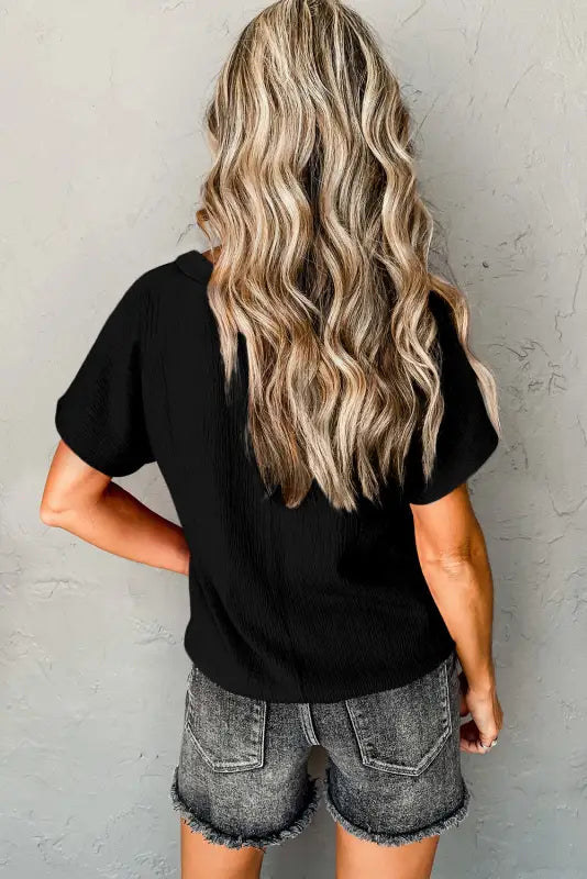 Long wavy blonde hair in black crinkled v neck wide sleeve t-shirt and denim shorts