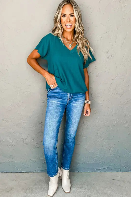 Smiling woman with long blonde hair, wearing a teal t-shirt and blue jeans