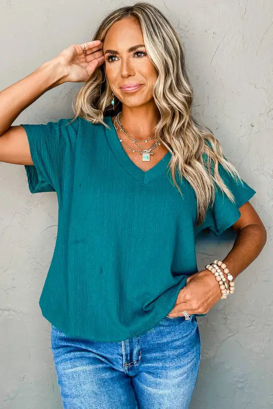 Woman in teal v-neck top and jeans, showcasing black crinkled v neck wide sleeve t-shirt