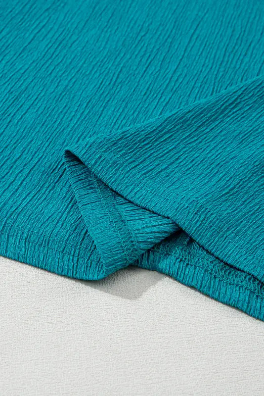 Teal textured fabric with folded corner from black crinkled v neck wide sleeve t-shirt