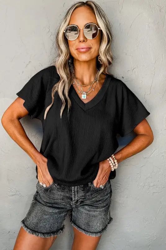 Woman with blonde hair in sunglasses, denim shorts, and a black crinkled v neck t-shirt