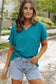 Woman in teal v-neck shirt and denim shorts showcasing black crinkled v neck wide sleeve t-shirt