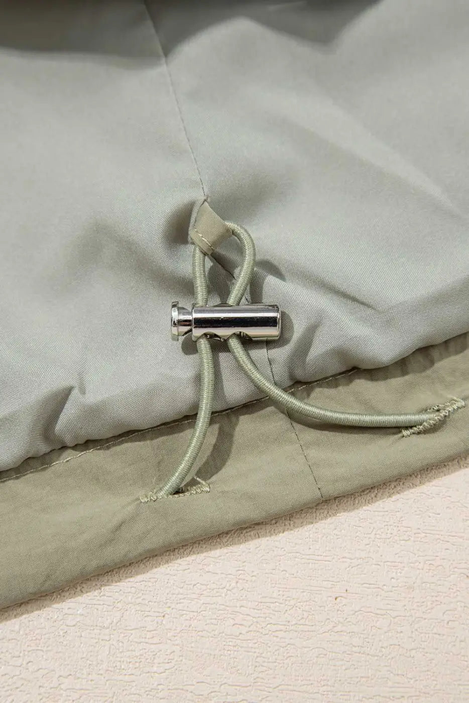 Interior drawstring toggle of Cropped Hooded Utility Jacket in laurel green, highlighting adjustable fit and casual utility style.